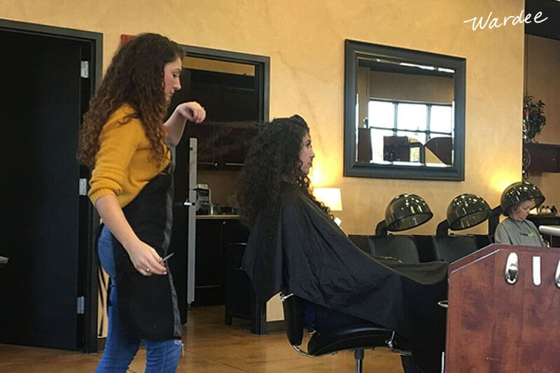 hairdresser giving a woman with dark curly hair a haircut