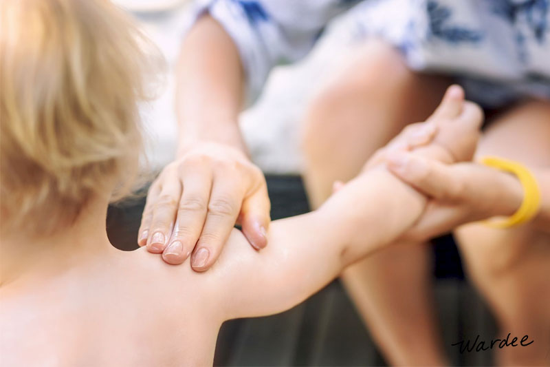 Mother applying sunscreen onto her small child's bare shoulders.