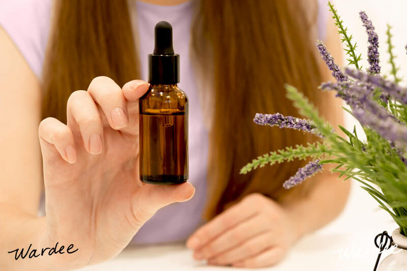 Woman holding up an amber-colored dropper bottle of hair oil.