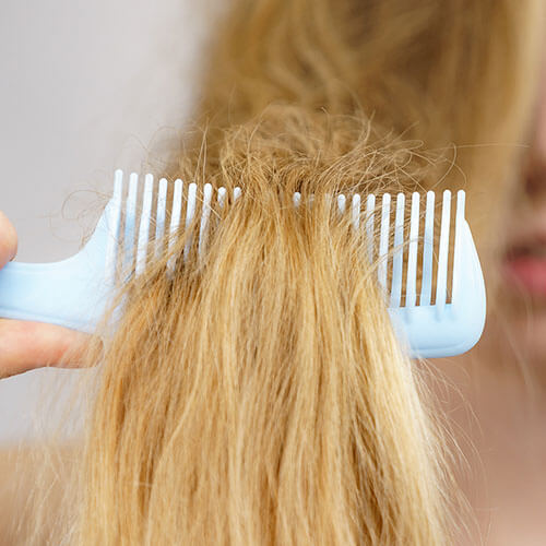Close-up shot of a wide tooth comb running through a person's blonde, dry hair.