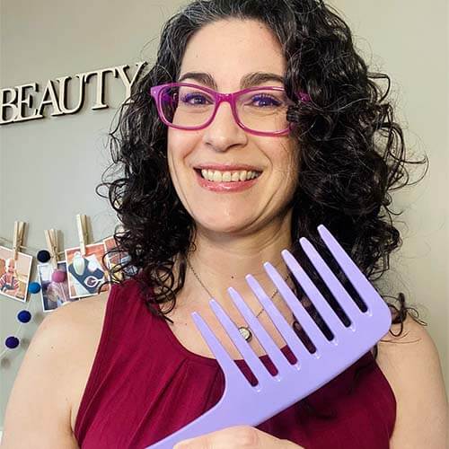 Photo of smiling woman with dark curly hair holding up a purple wide tooth comb