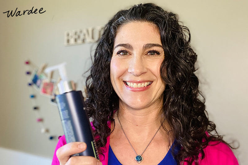 Smiling woman holding up a bottle of clarifying shampoo.