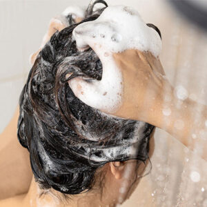 Woman washing her hair. Her hands are covered in suds.