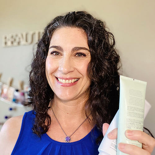Photo of a smiling woman holding up a bottle of exfoliating scrub.