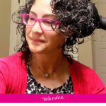 Smiling woman with bright pink glasses diffusing her hair until it is dry. Text overlay says: "How to Diffuse Hair for Volume At Roots (without having to tip head upside down... neck-safe routine)"