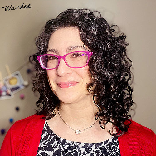 Smiling woman with dark curly hair and bright pink glasses.