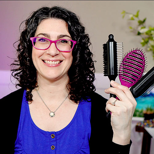 Photo of a smiling woman with curly hair, holding up various styling brushes.