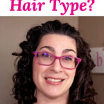Photo of a smiling woman with curly hair, wearing pink glasses. Text overlay says: "What Is Your Hair Type? (structure, density, porosity, curl type!)"