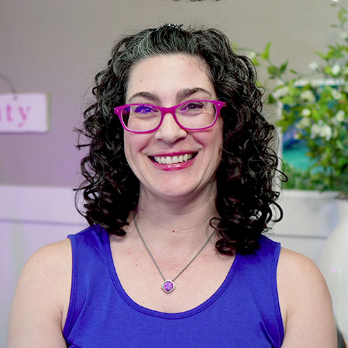 Smiling woman with curly hair and pink glasses.